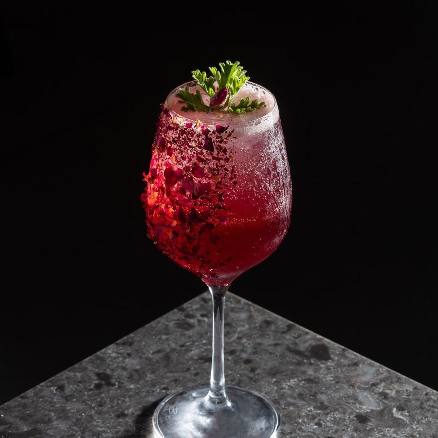 A red cocktail on a stone surface, backlit so the drink glows against a dark background