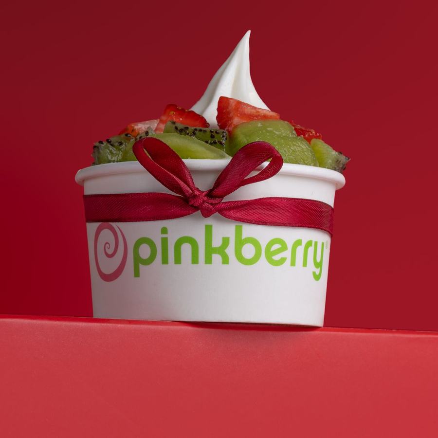A frozen yoghurt cup topped with fruit, lit cleanly against a saturated pink and red set