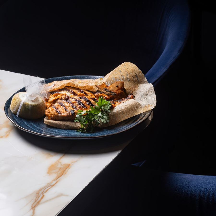 A grilled fillet on a dark plate, lit from the side against a black background